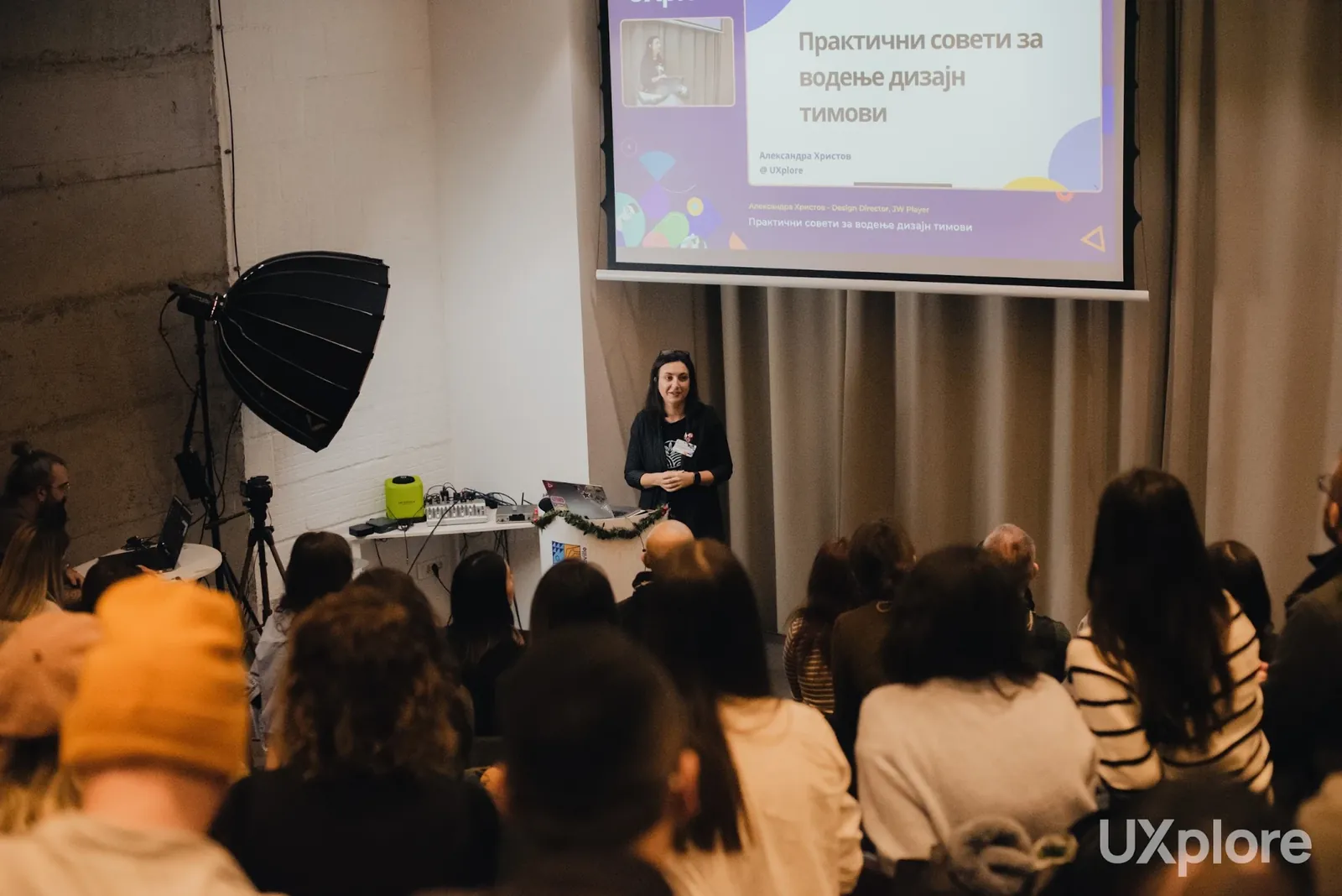 Aleksandra giving a talk to a seated audience at UXplore, in front of a projected slide titled “Practical advice for leading design teams”, in Macedonian.